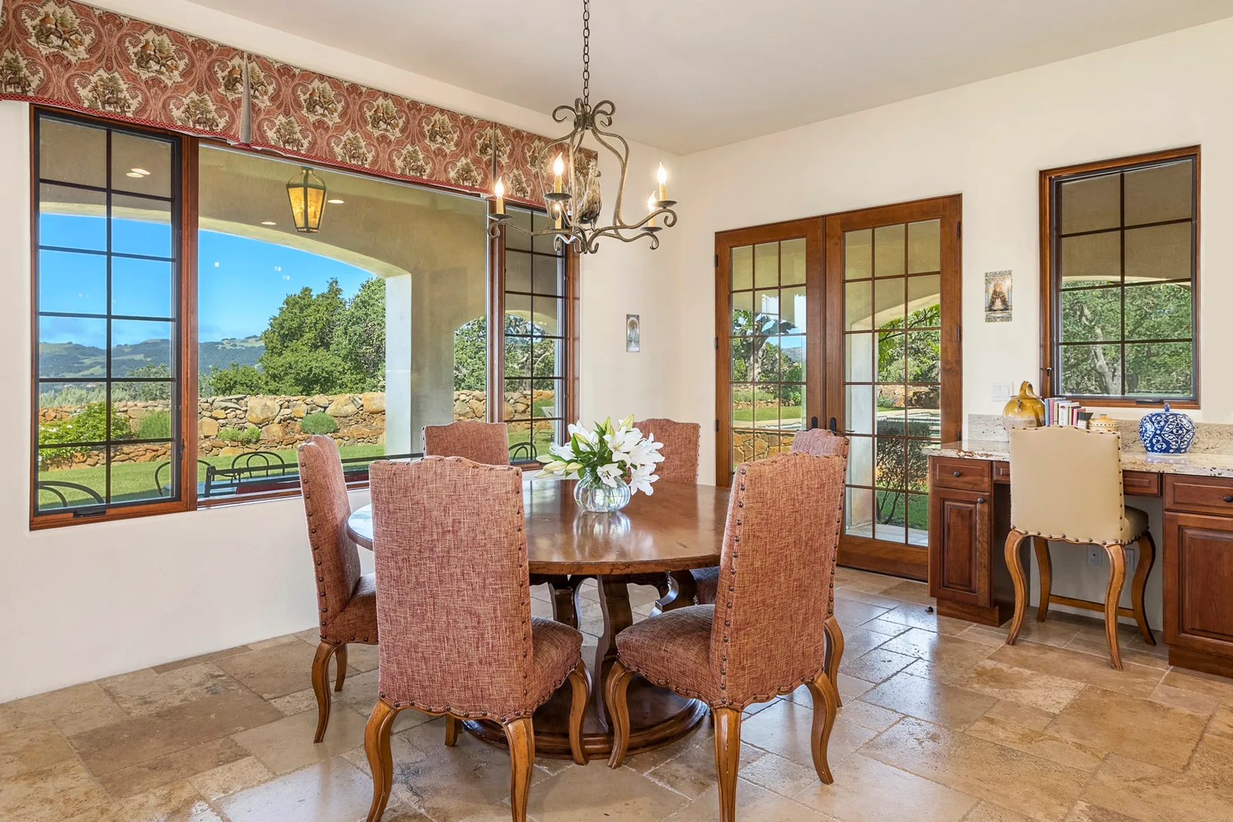 A dining room with a wooden table and chairs beside large windows.