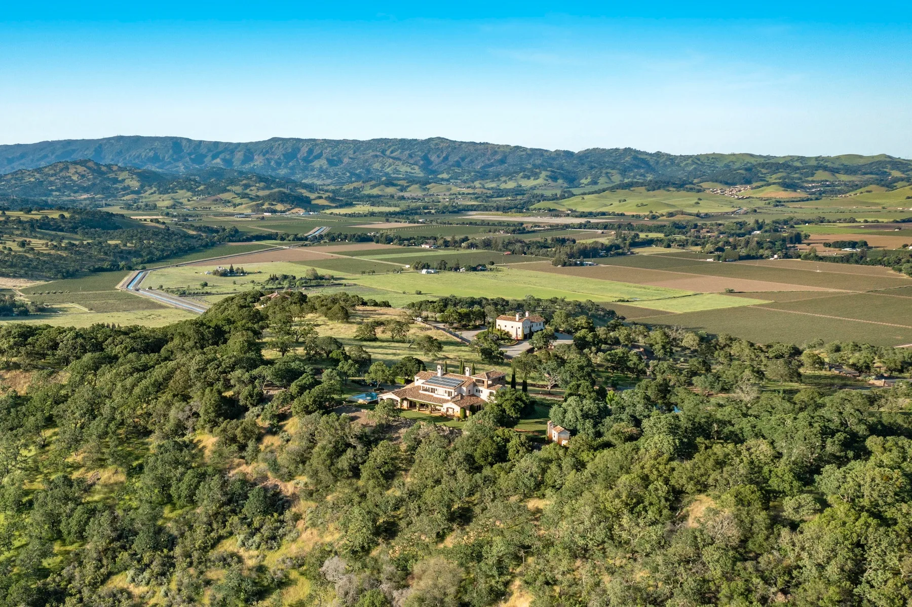 Aerial landscape view of a wooded estate amid fields and distant hills.
