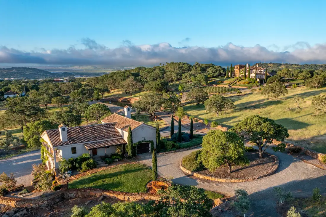 Aerial view of a countryside property with buildings, trees, and surrounding hills.