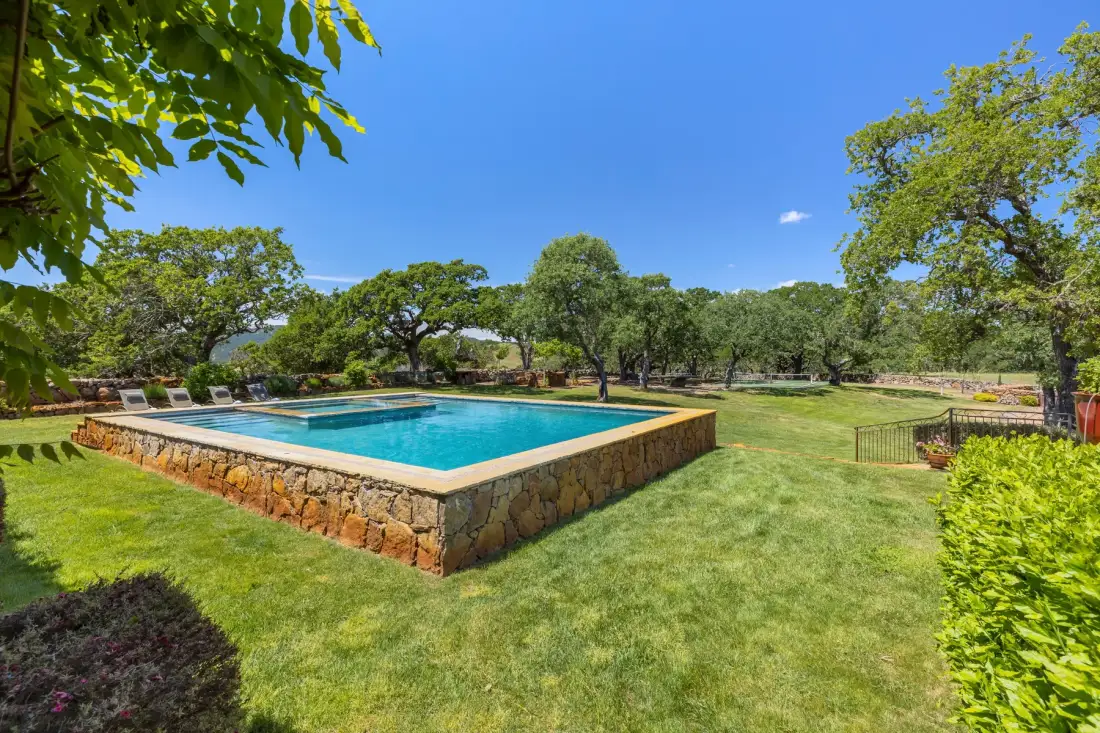 A swimming pool sits in a grassy garden surrounded by trees.
