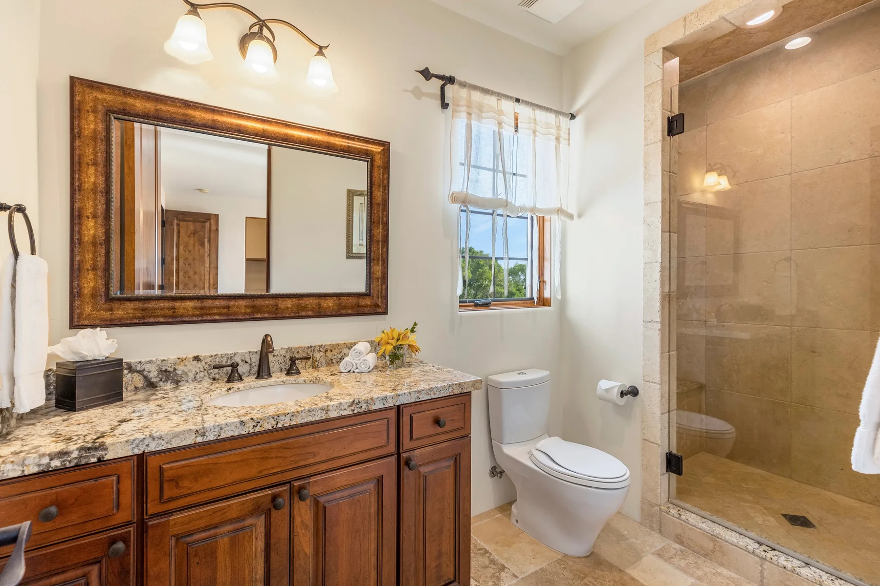 A bathroom with a wood vanity, mirror, window, and glass shower.