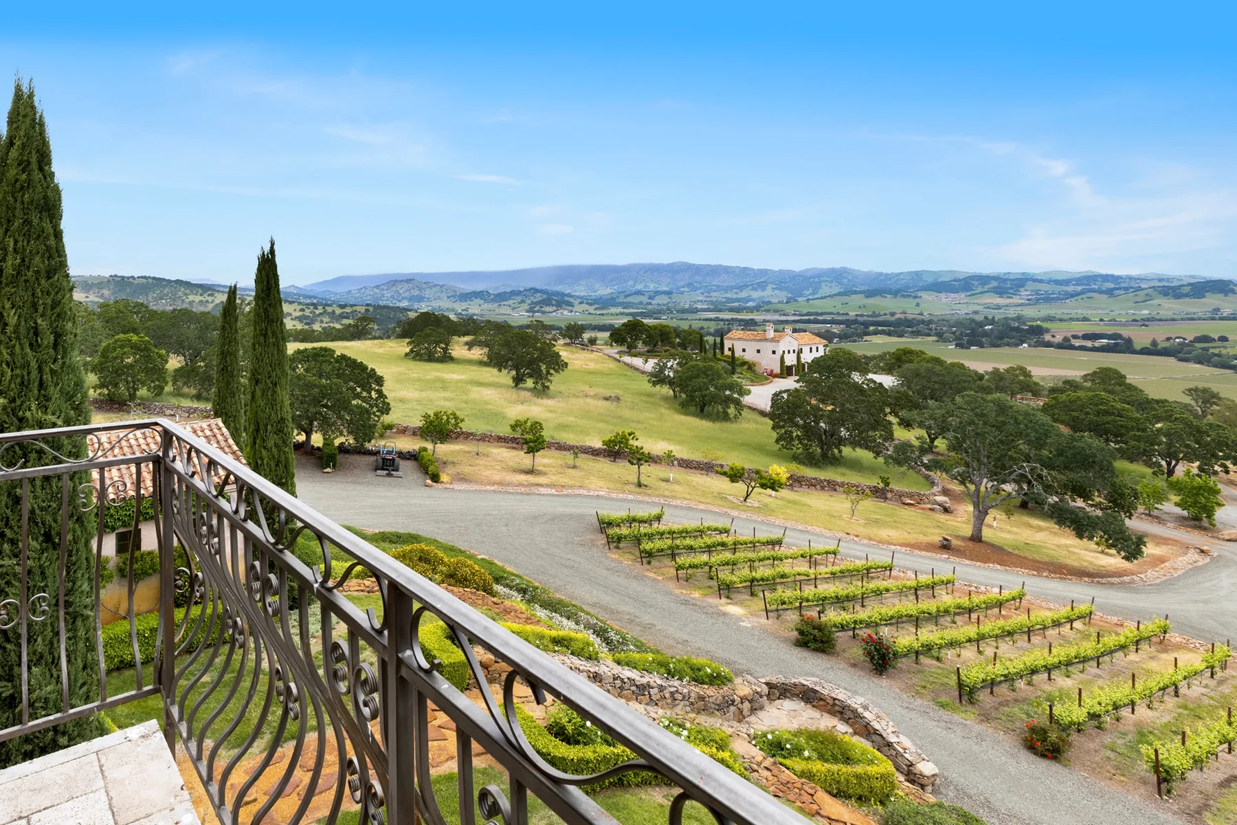 A balcony overlooks a vineyard and rolling countryside beneath a clear sky.