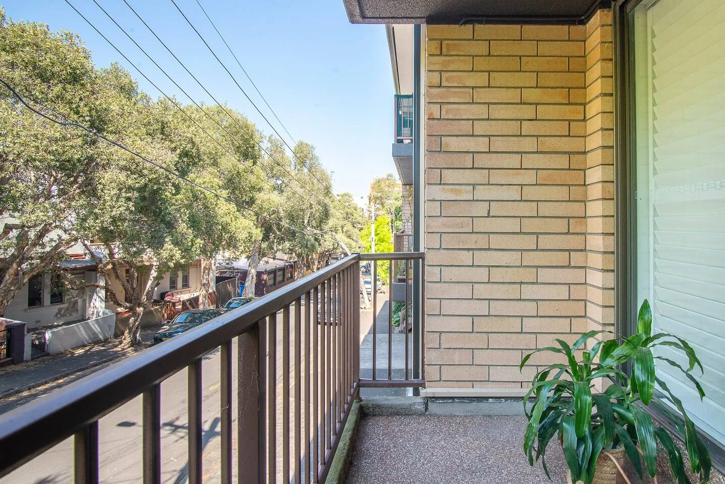 A balcony overlooks a tree-lined street beside a brick wall.