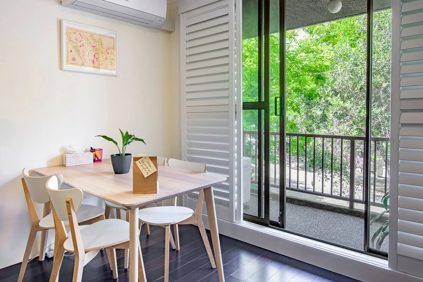Una zona de comedor con mesa y sillas está junto a puertas correderas abiertas que dan a una frondosa vegetación.
