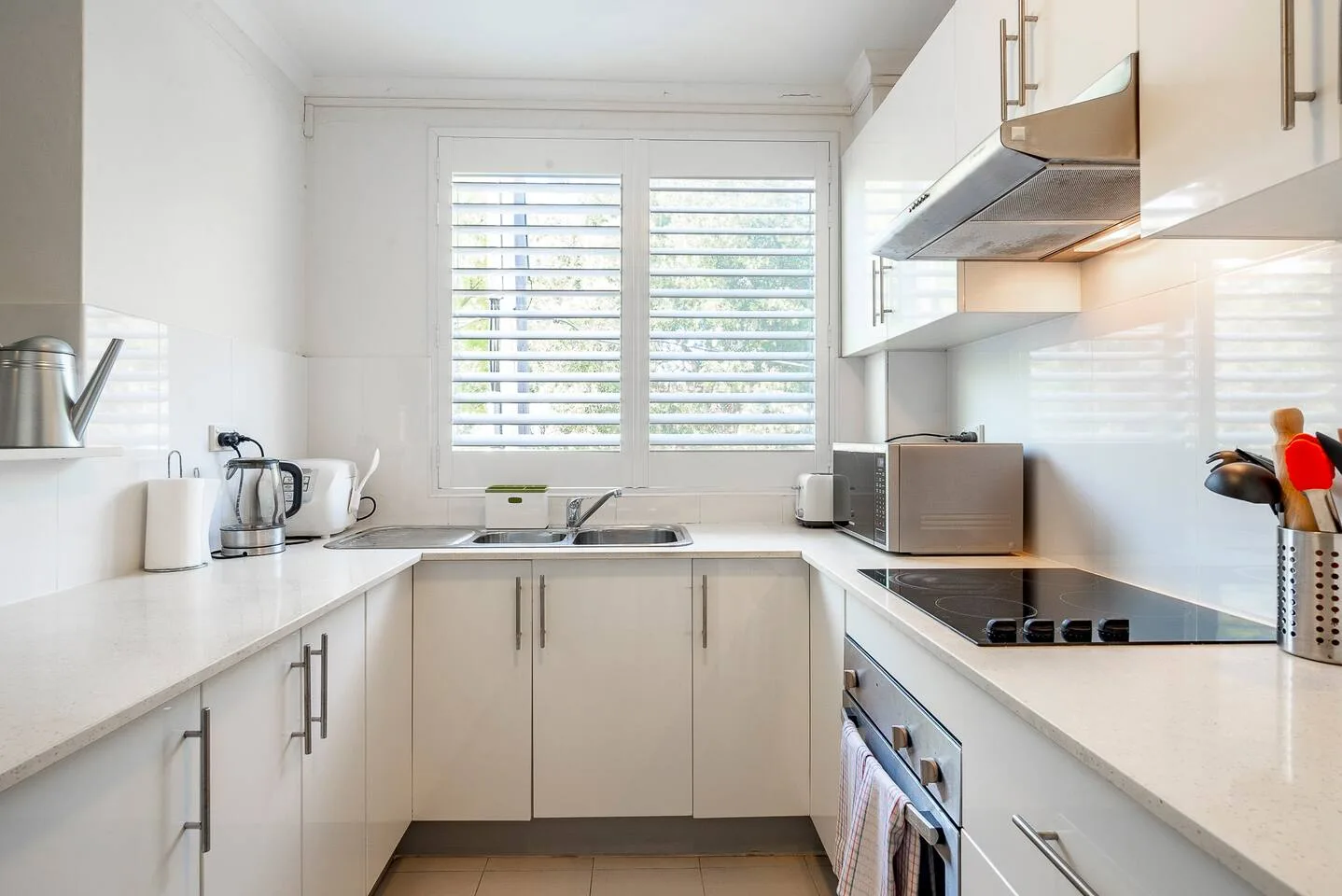 Una cocina luminosa con armarios blancos, encimeras y una ventana sobre el fregadero.