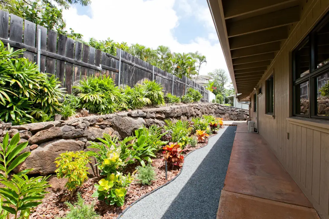 Un pasillo exterior cubierto bordea un jardín ajardinado y un muro de piedra.