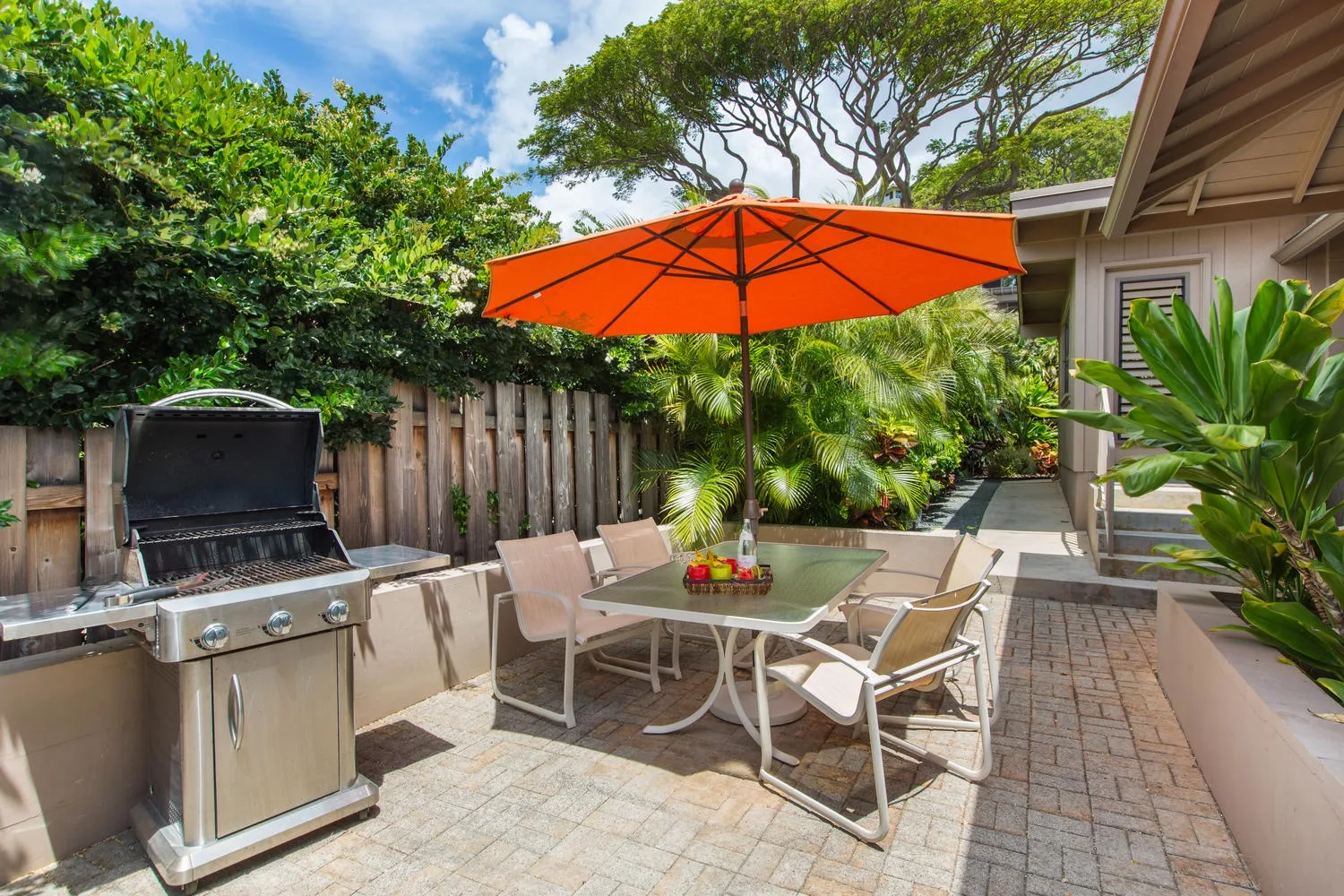 An outdoor patio with a dining table beneath an orange umbrella.