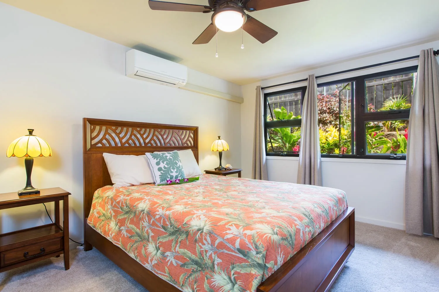 Un dormitorio con cama de madera, ropa de cama floral colorida y una ventana con vegetación.