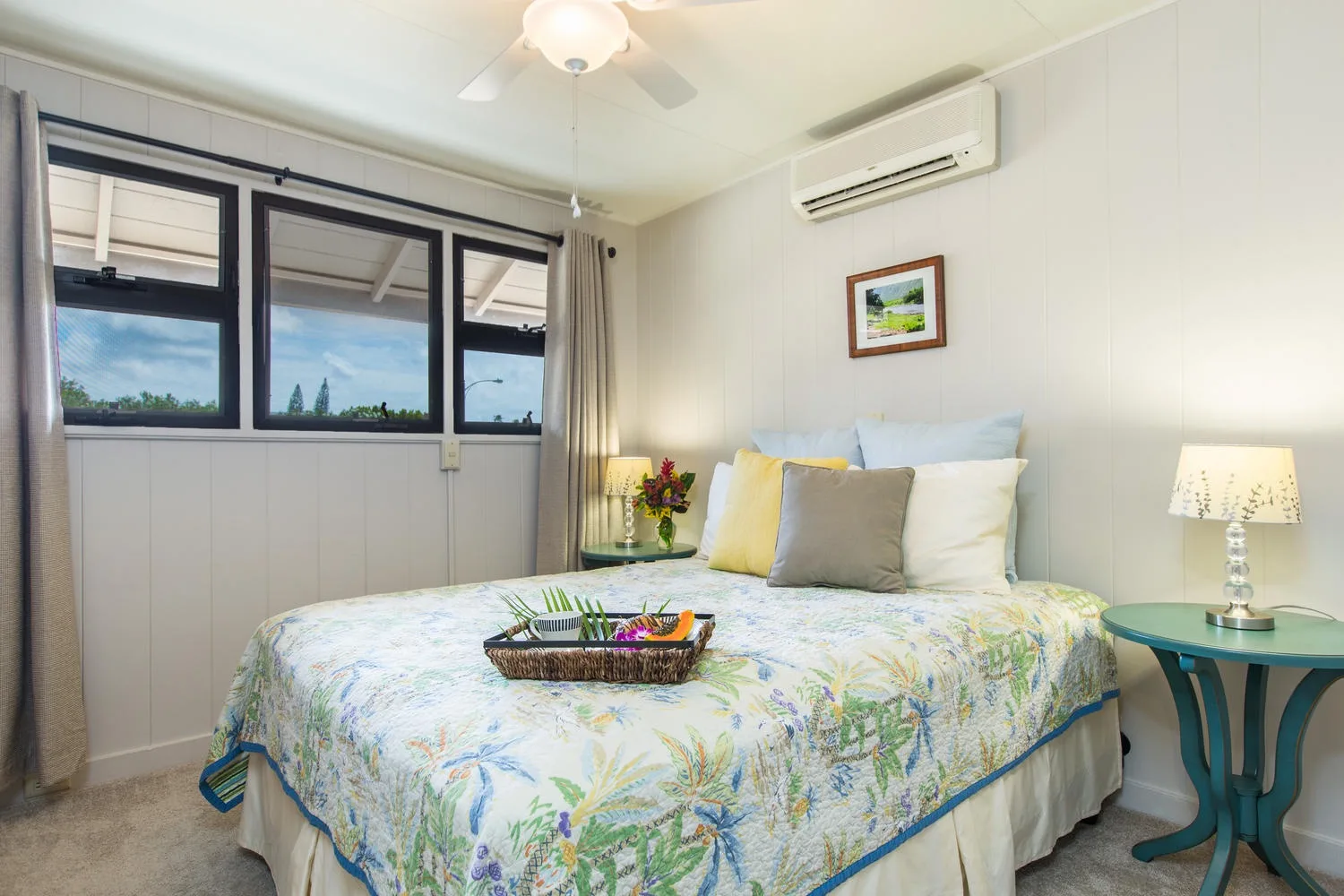 Un dormitorio con una cama cubierta con un estampado floral junto a grandes ventanas.