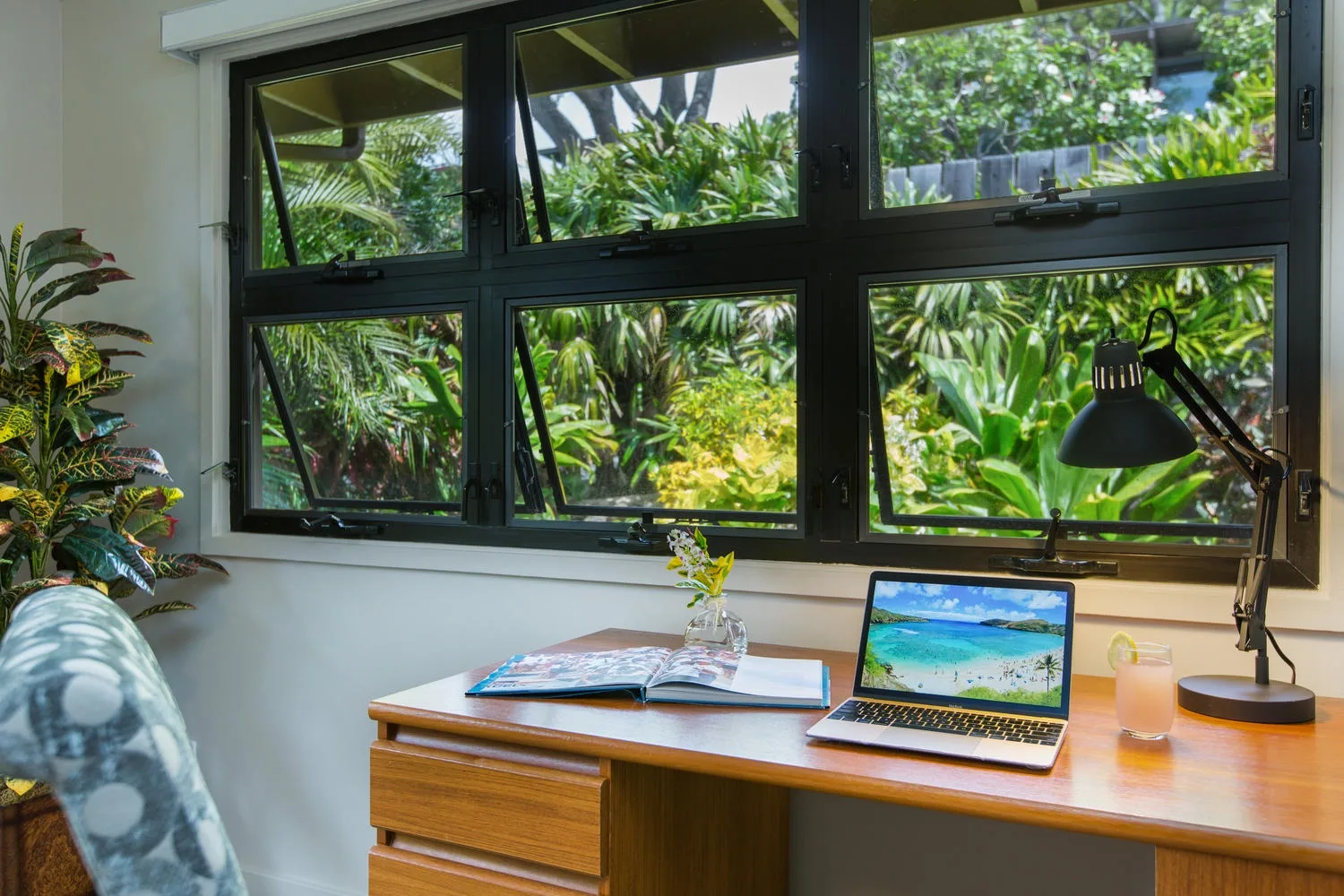 Un escritorio está bajo una amplia ventana con vistas a una vegetación frondosa.