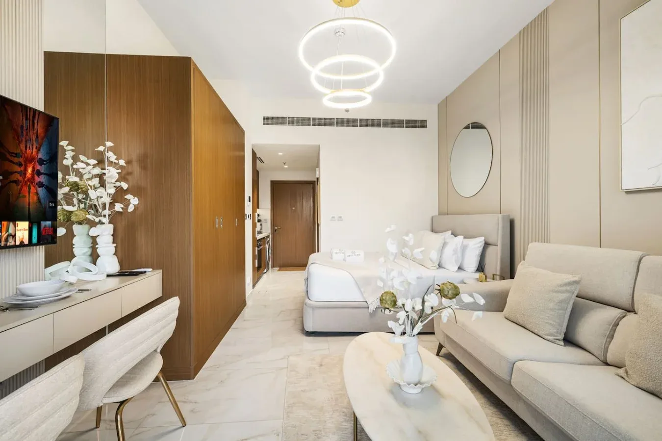 Una sala luminosa con asientos claros, una mesa de centro y un gran armario de madera.