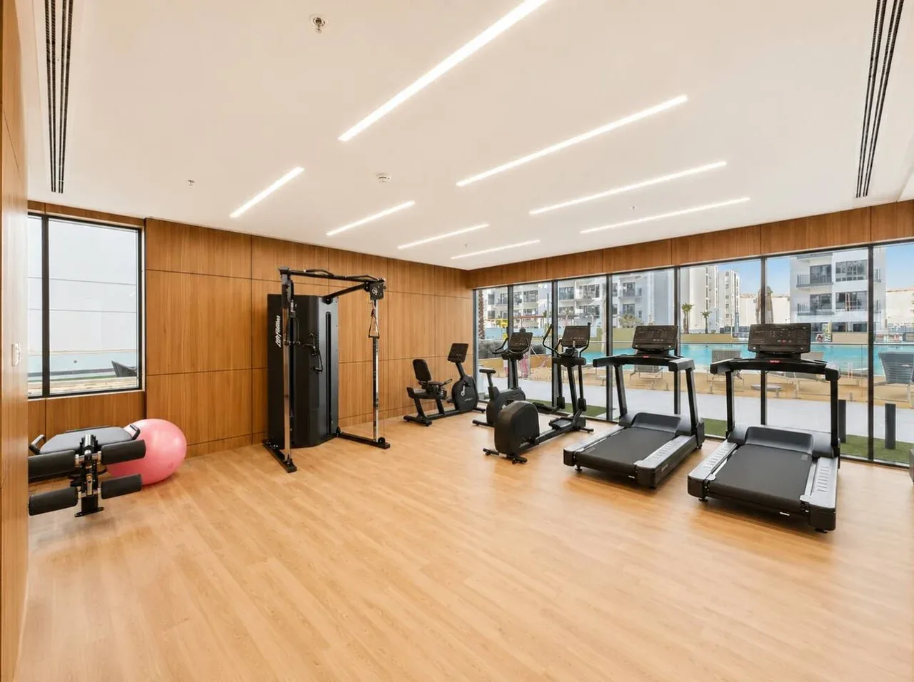 Un gimnasio luminoso con equipos de ejercicio junto a ventanas de piso a techo.
