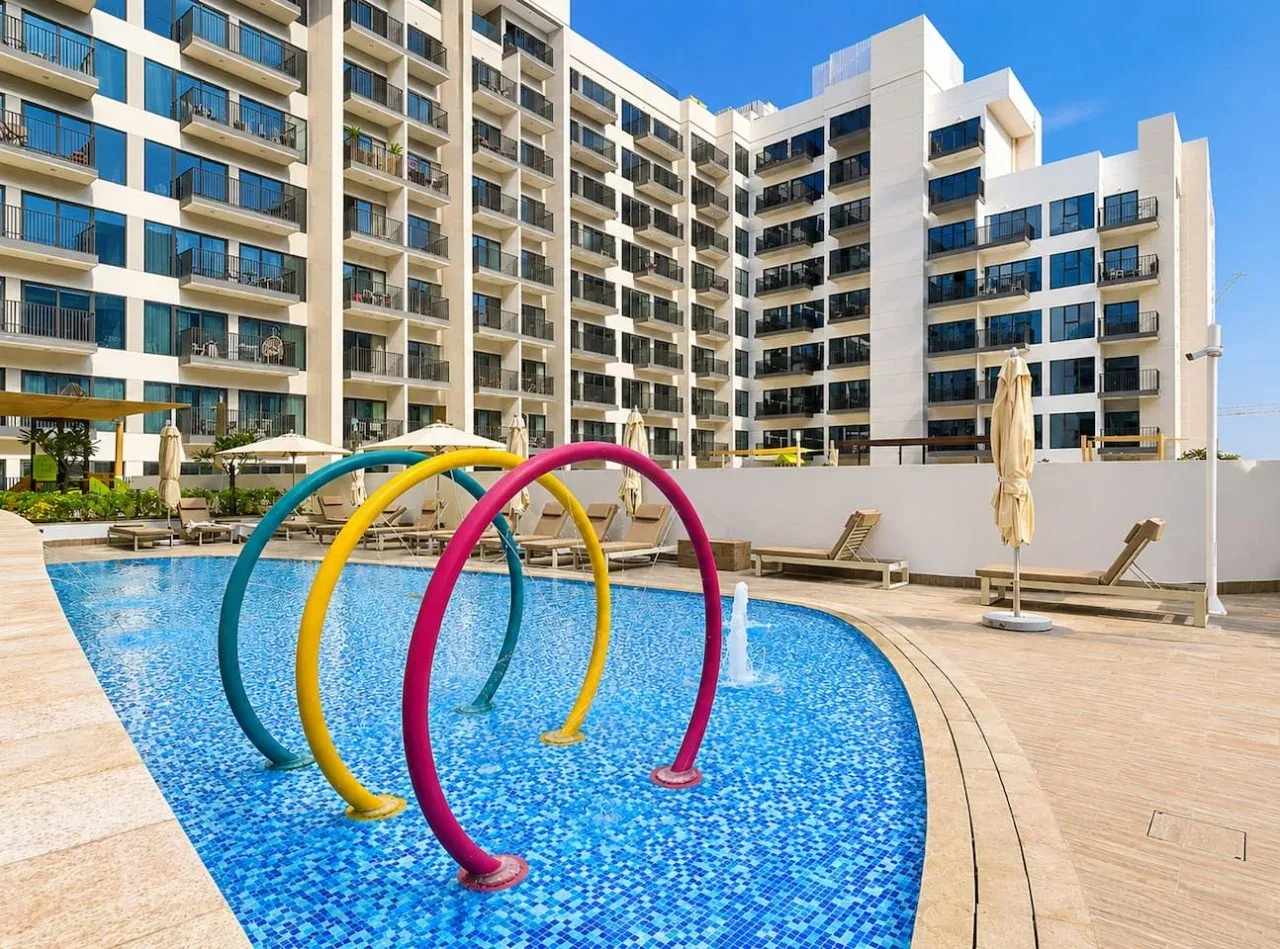 Una piscina con elementos curvos de colores junto a un edificio de apartamentos moderno.