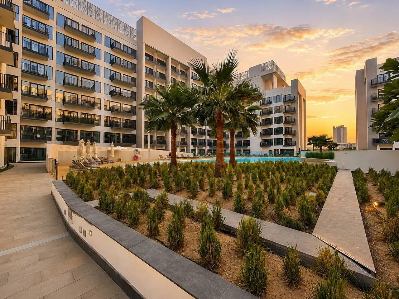 Un patio ajardinado con palmeras y una piscina entre edificios modernos.