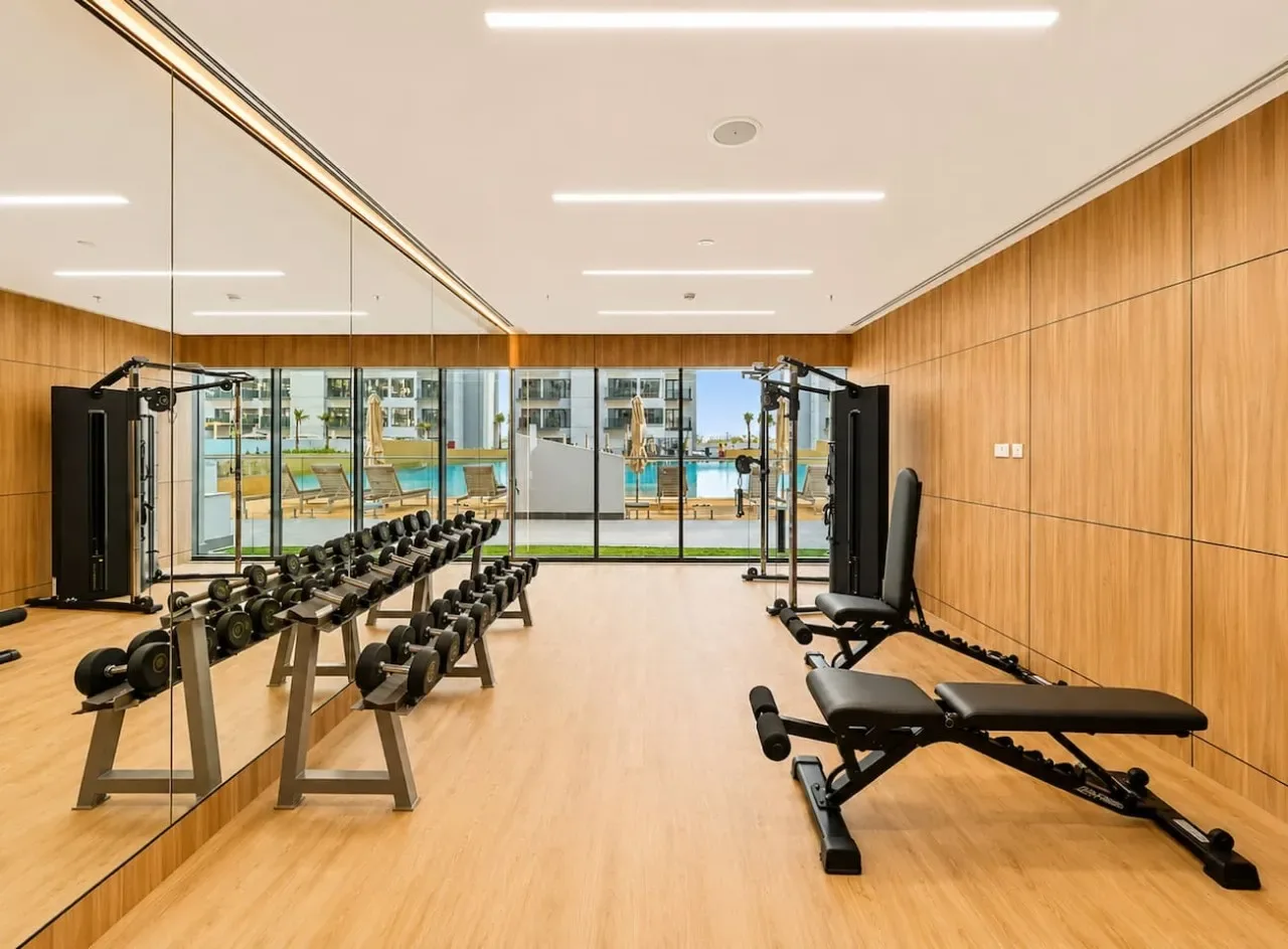 Un gimnasio con una pared de espejos, soportes para pesas y bancos de ejercicio.