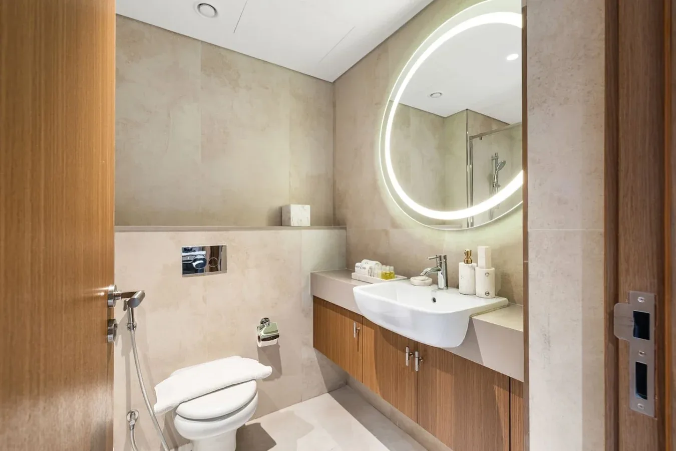 Un baño con lavabo, inodoro y espejo redondo iluminado.