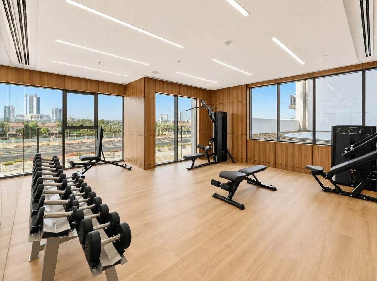 Sala de ejercicio con máquinas y grandes ventanales con vistas a la ciudad.