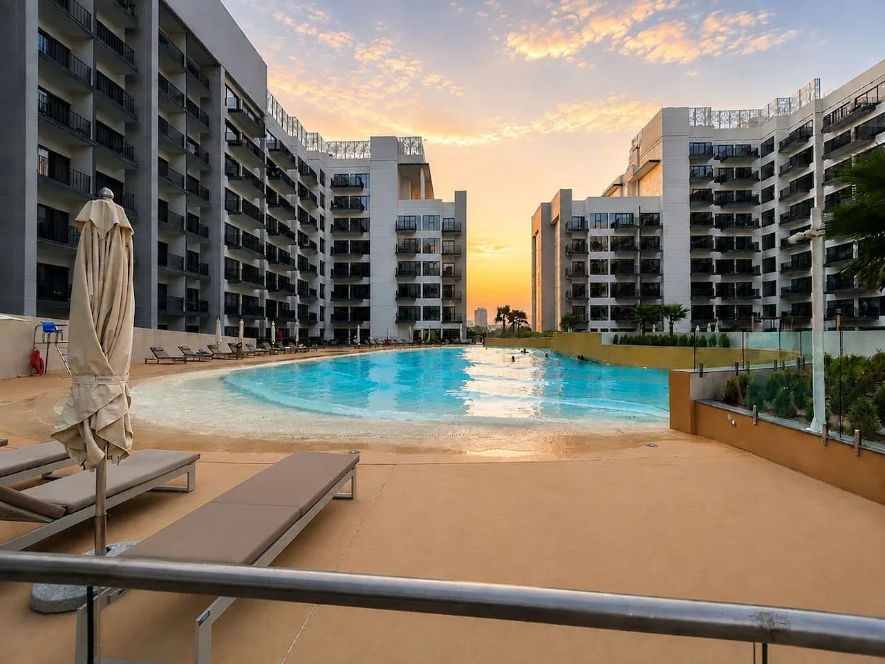 Una piscina al aire libre se encuentra entre edificios modernos bajo el cielo del atardecer.