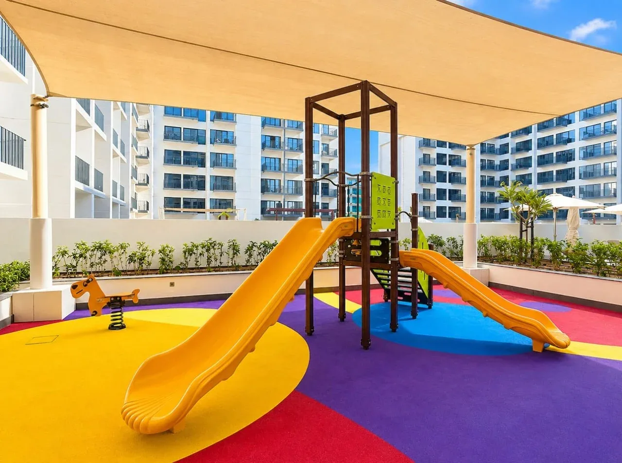 Un colorido parque infantil al aire libre con toboganes y juegos bajo una cubierta de sombra.