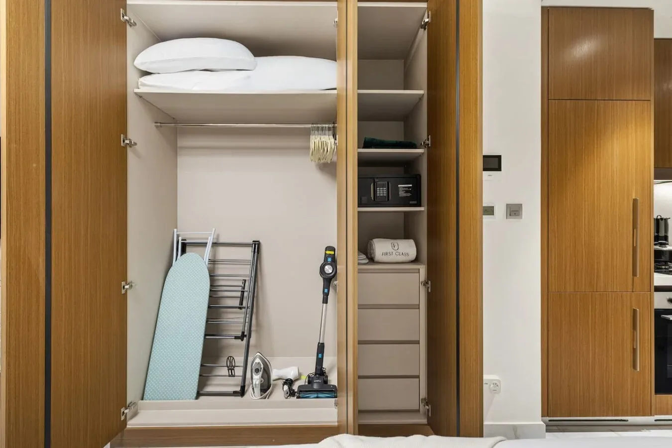 Un armario empotrado abierto contiene ropa de cama doblada, una tabla de planchar y equipo de limpieza.