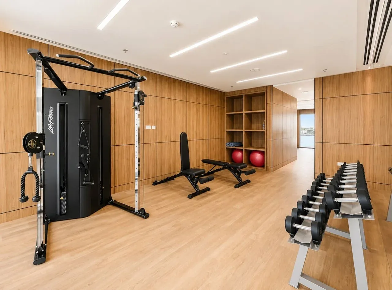 Un gimnasio compacto con máquinas de pesas, un banco y una fila de mancuernas.