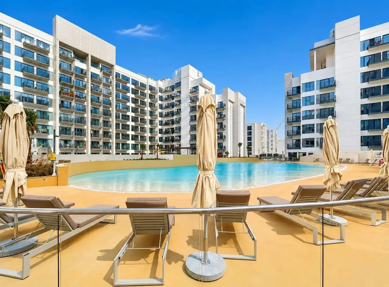 Una piscina está rodeada de tumbonas y edificios modernos de apartamentos.