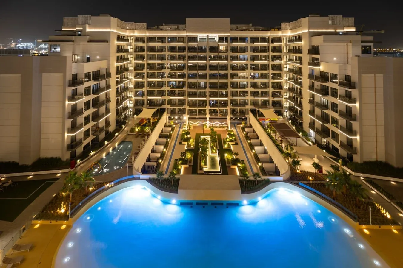 Un gran edificio iluminado se alza detrás de una piscina azul brillante por la noche.