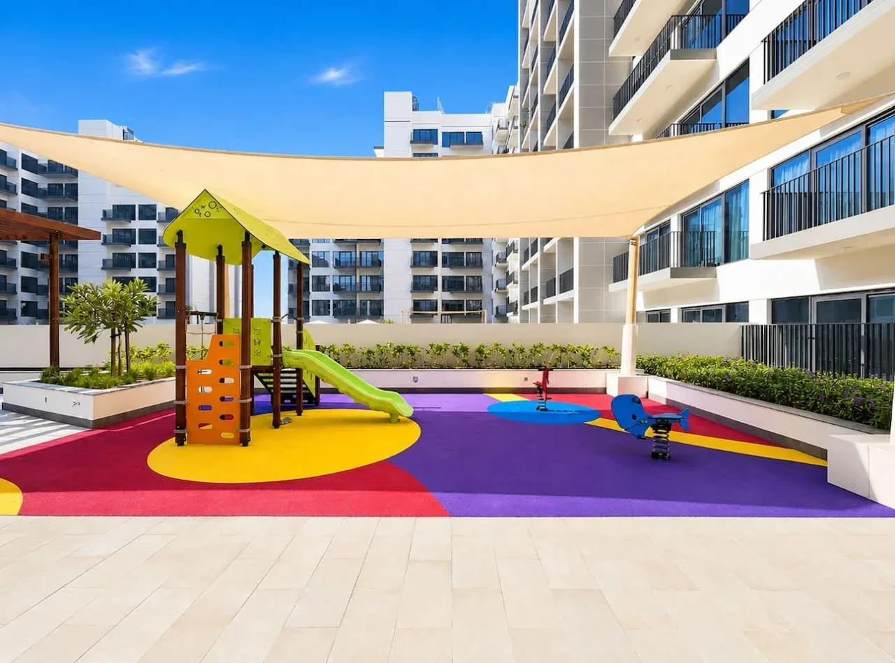 Un parque infantil colorido está bajo una cubierta de sombra en un patio.