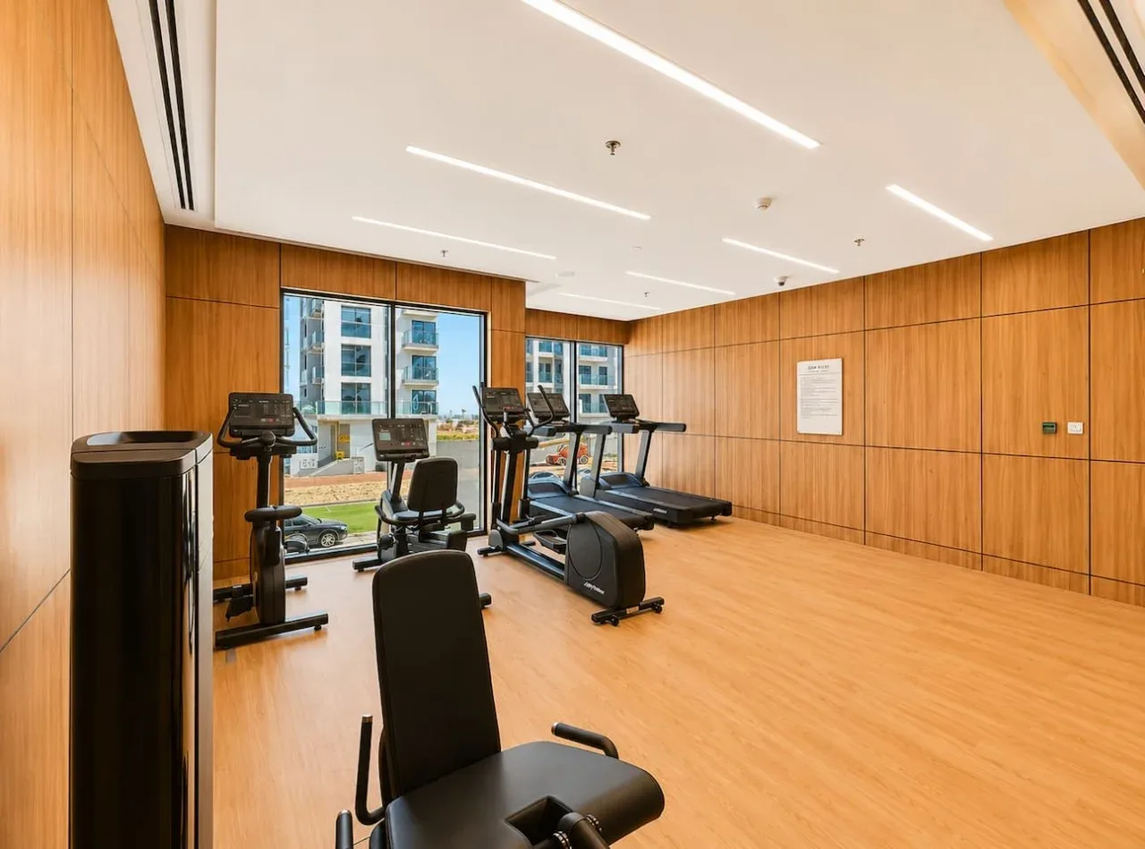 Un gimnasio luminoso con máquinas de ejercicio y grandes ventanas.