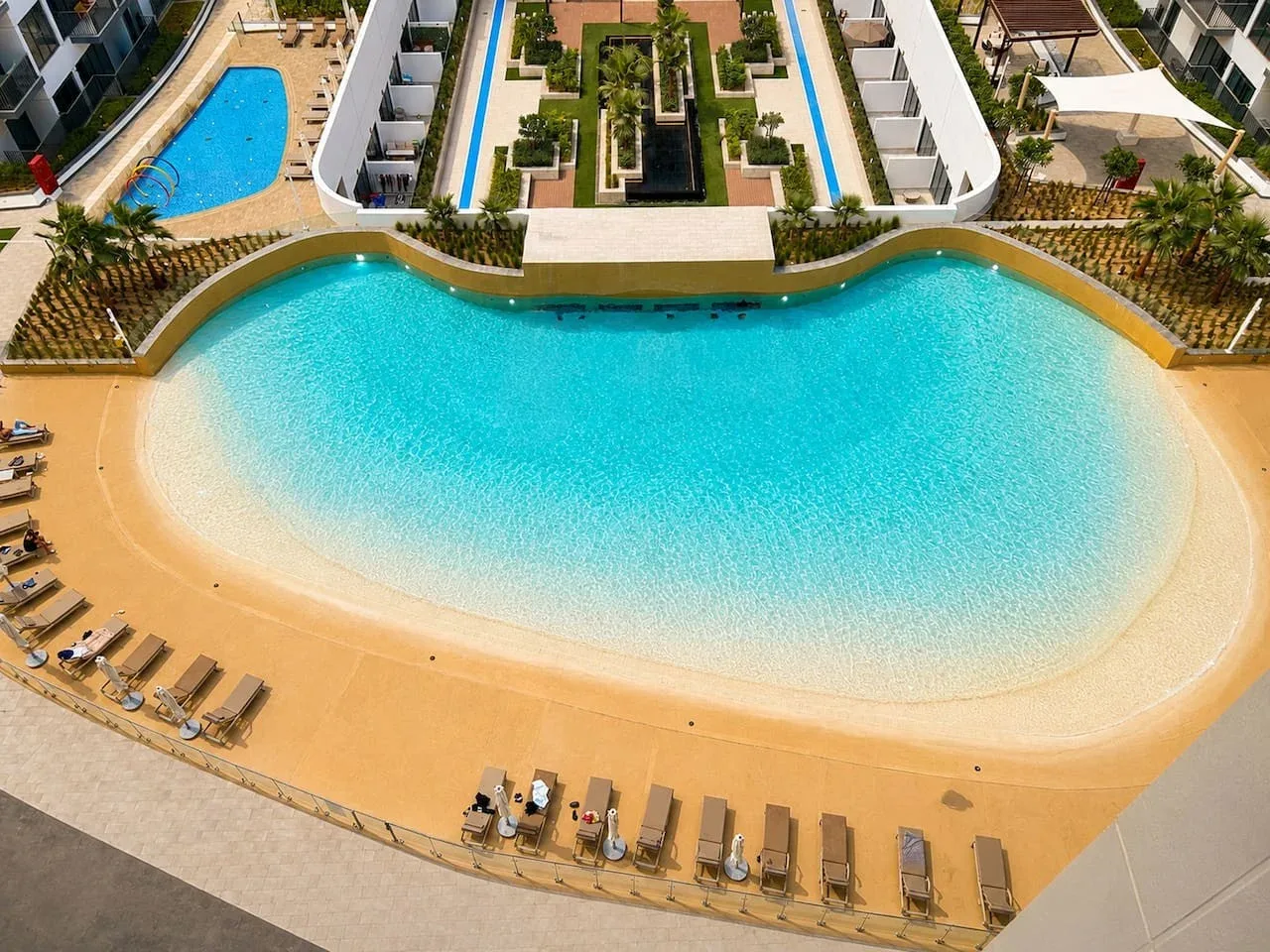 Una amplia piscina con una terraza de tono arena y filas de tumbonas.
