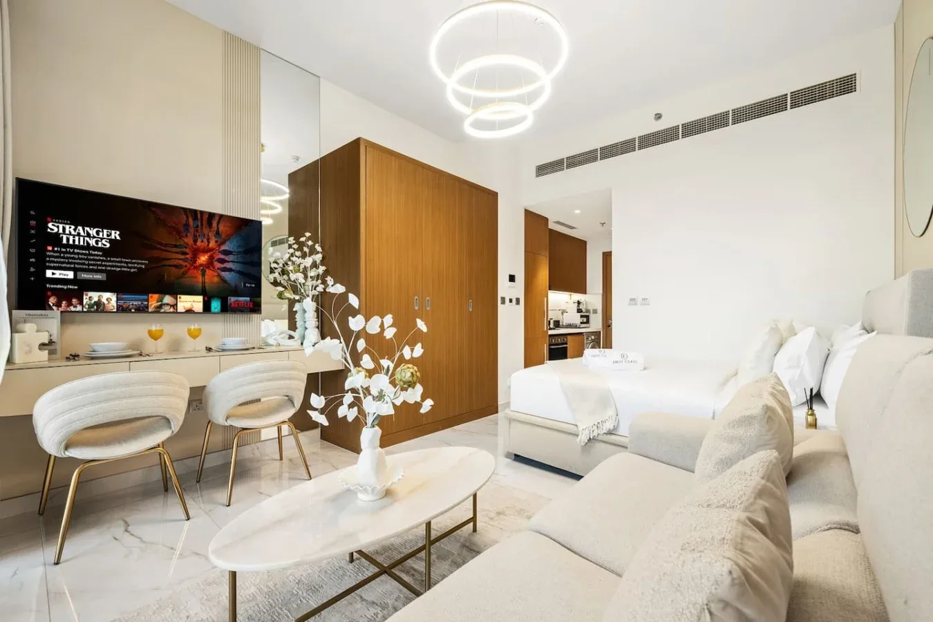 Una sala luminosa con asientos blancos, un televisor y un armario de madera.