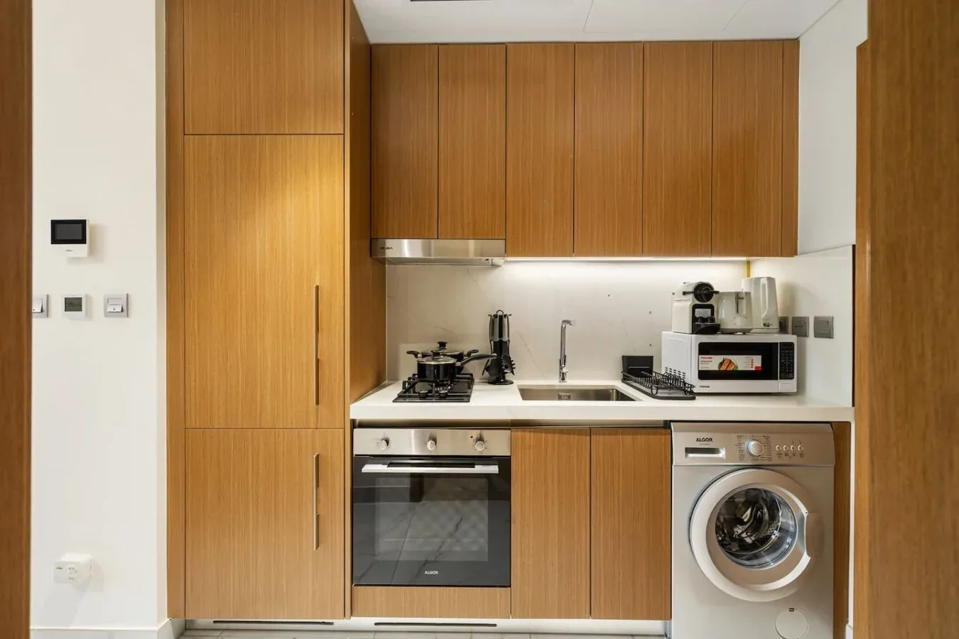 Una cocina compacta con armarios de madera, horno y lavadora.