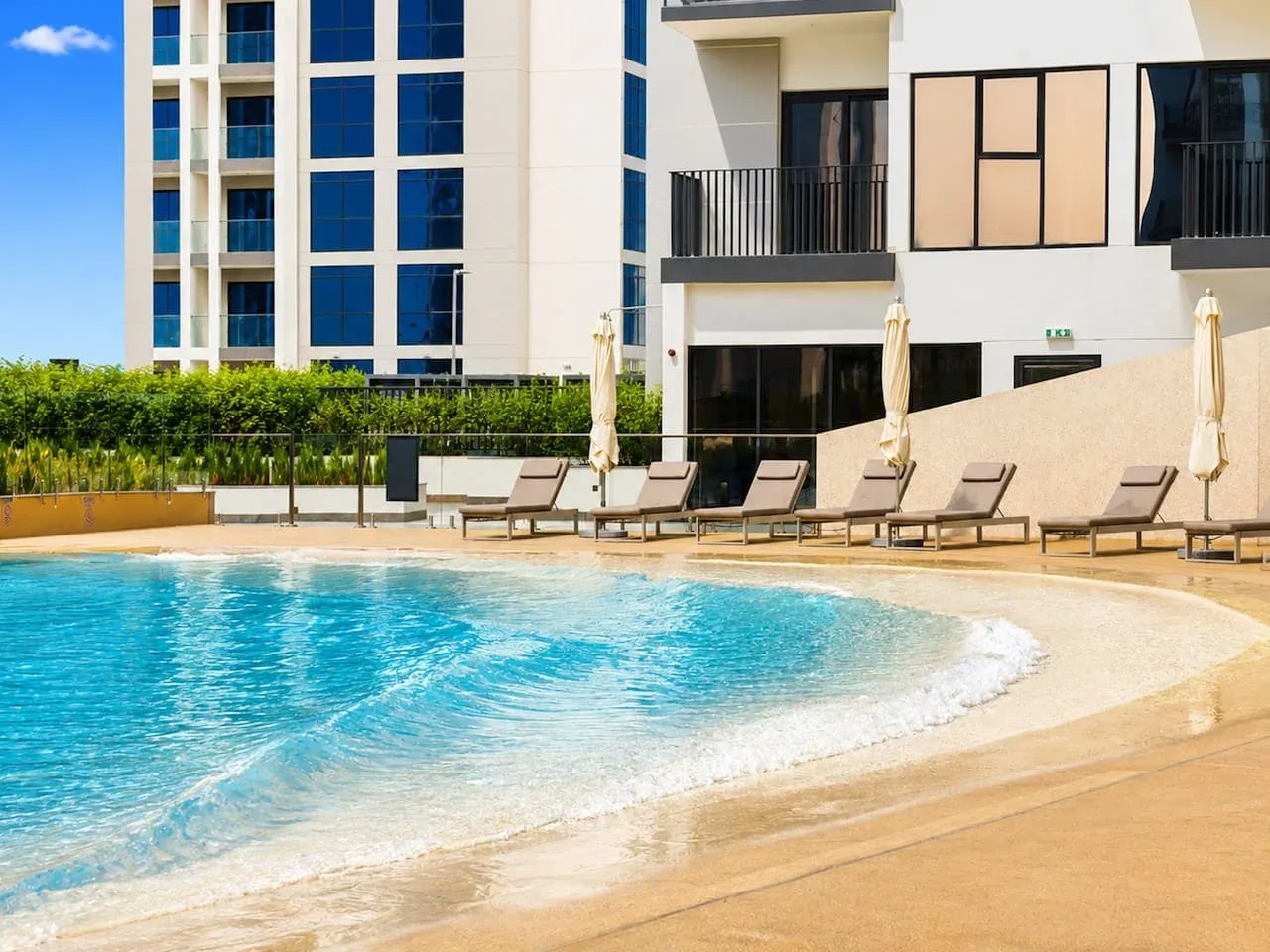 Una piscina al aire libre junto a un edificio moderno, con tumbonas junto al borde.