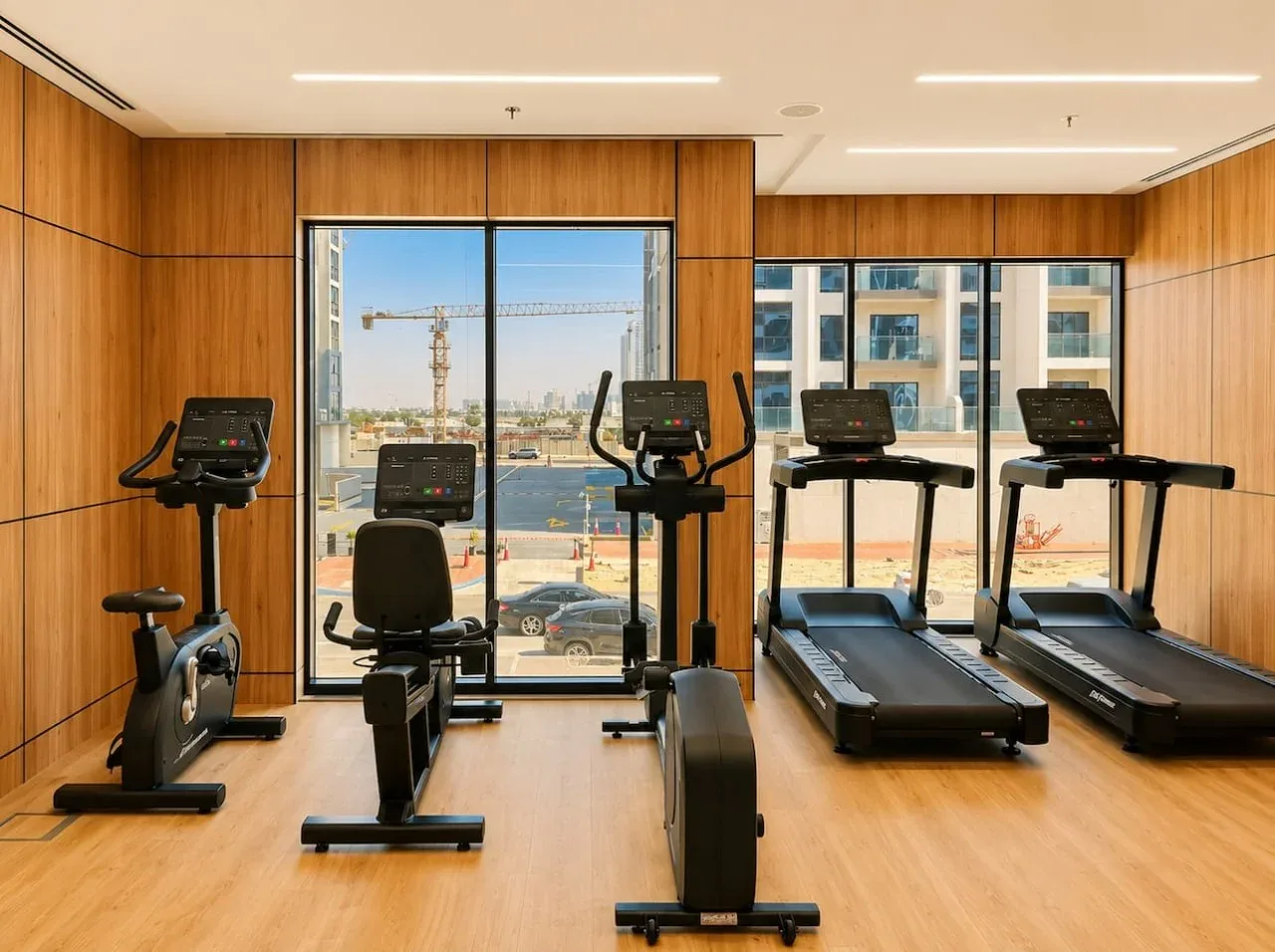 Un pequeño gimnasio con bicicletas estáticas y cintas de correr junto a grandes ventanas.