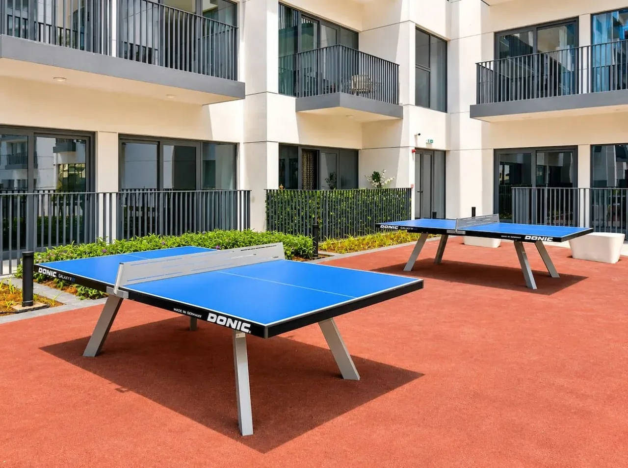 Zona recreativa al aire libre con mesas azules de ping-pong junto a un edificio moderno.
