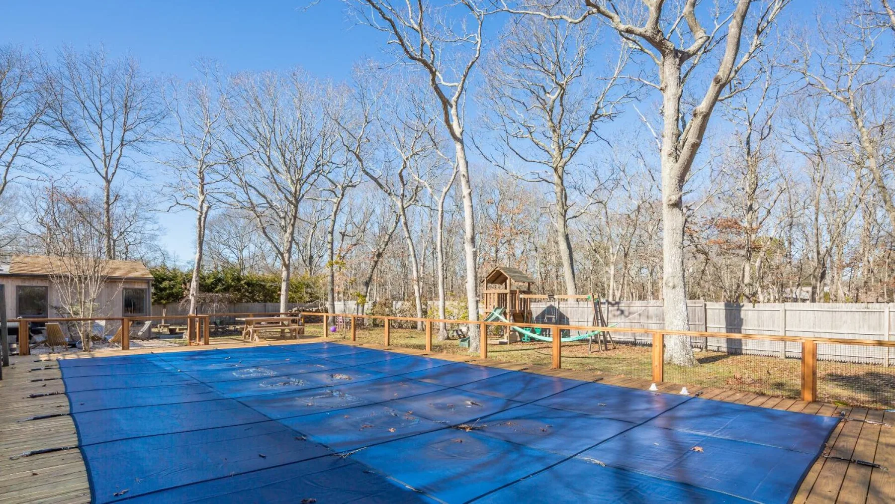 Una cubierta azul ocupa una piscina al aire libre rodeada de árboles.