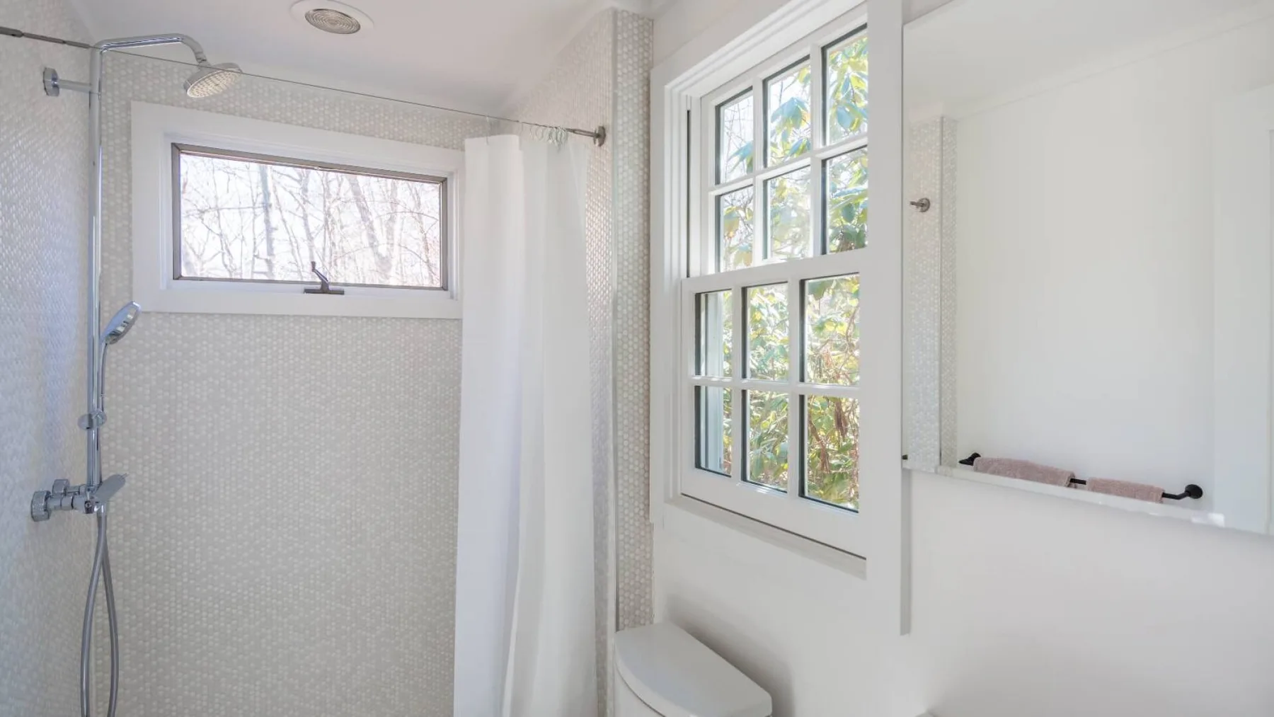 Un baño luminoso con ducha, bañera y ventanas grandes.