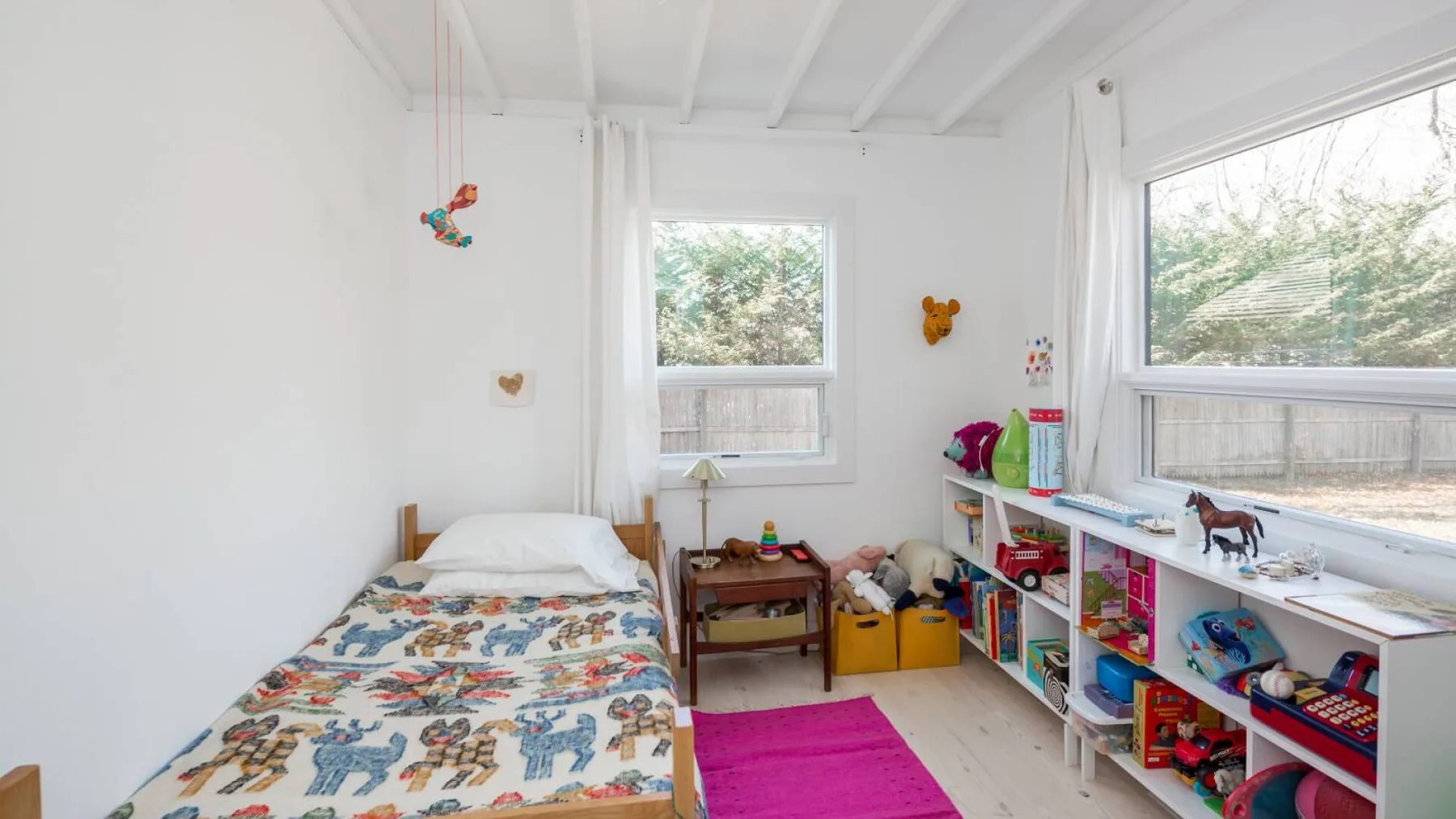 Un dormitorio infantil luminoso con una cama individual y estantes llenos de juguetes.
