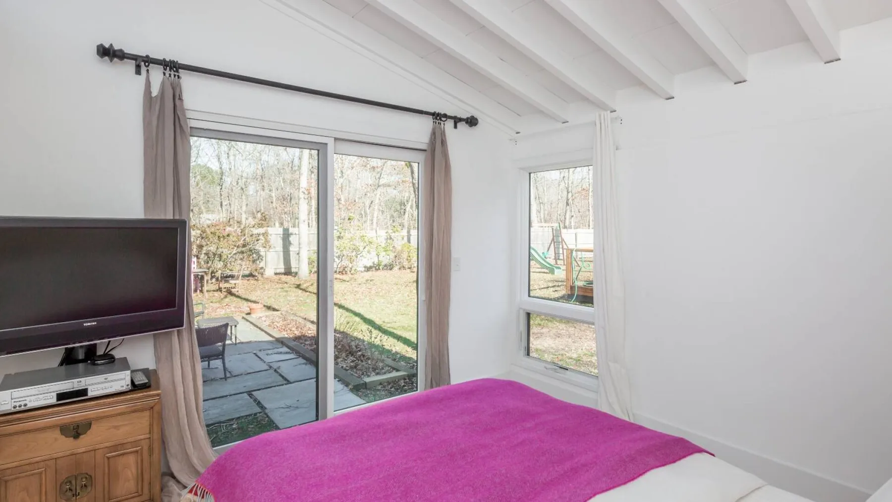 Un dormitorio con una cama cubierta con una manta rosa junto a unas puertas de vidrio.