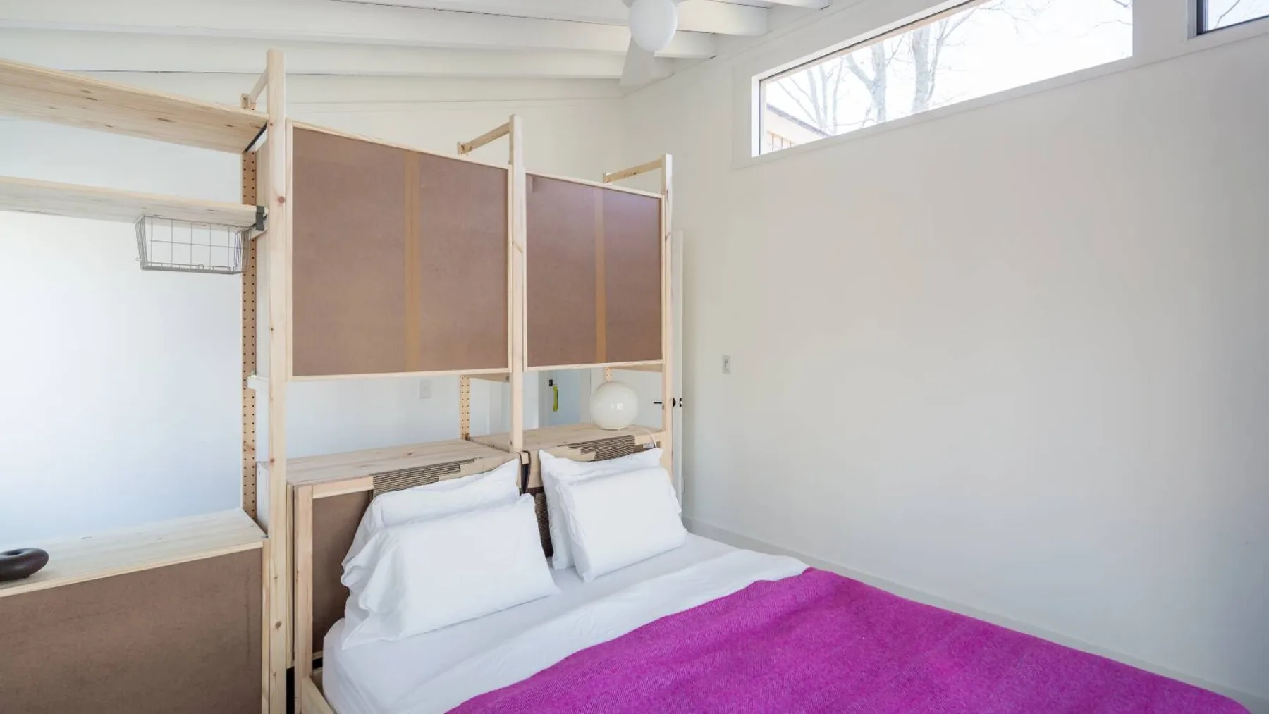 Un dormitorio con una cama, almohadas blancas y una colcha magenta brillante.