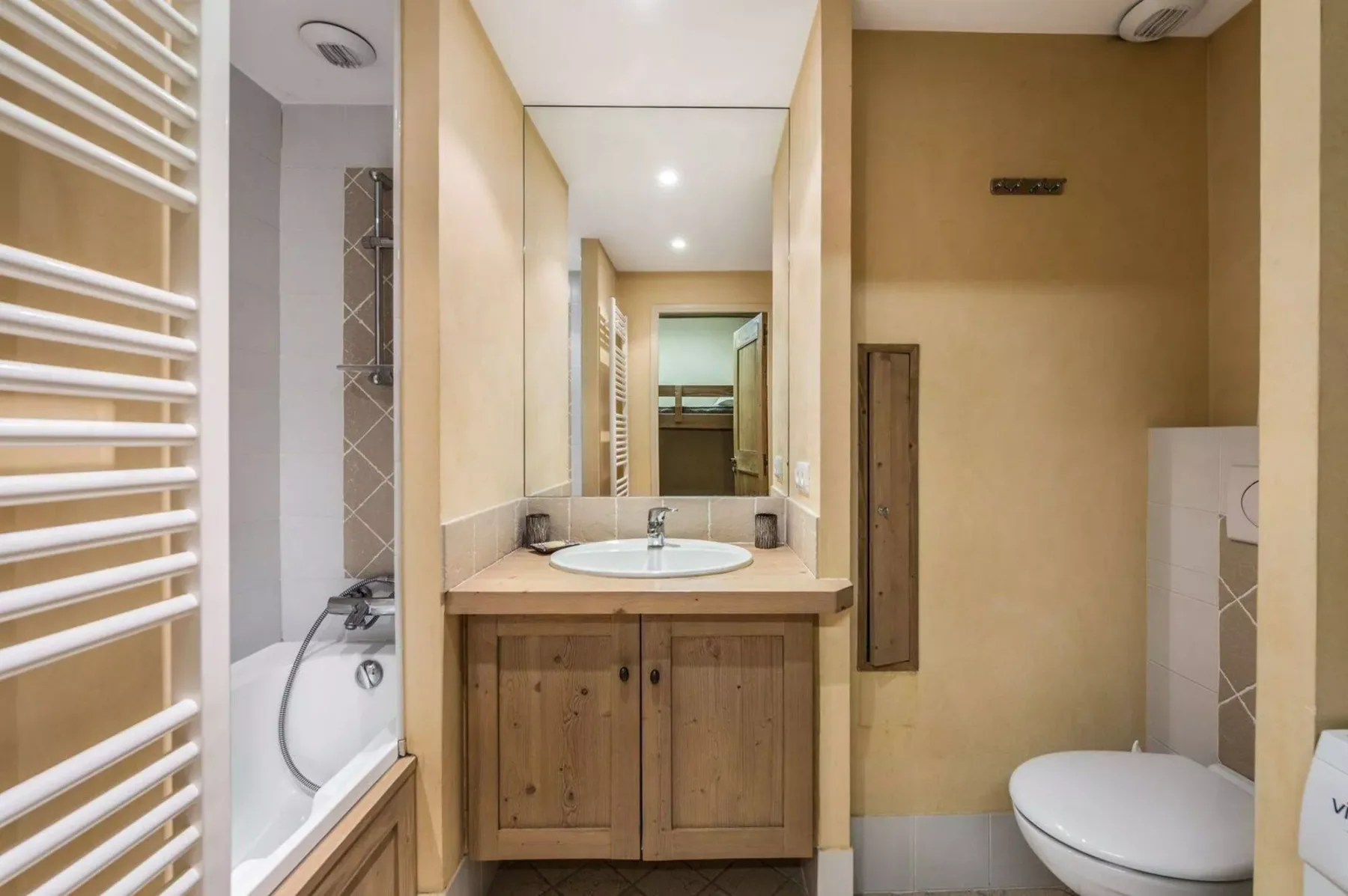 A bathroom with a sink and mirror between a bathtub and toilet.