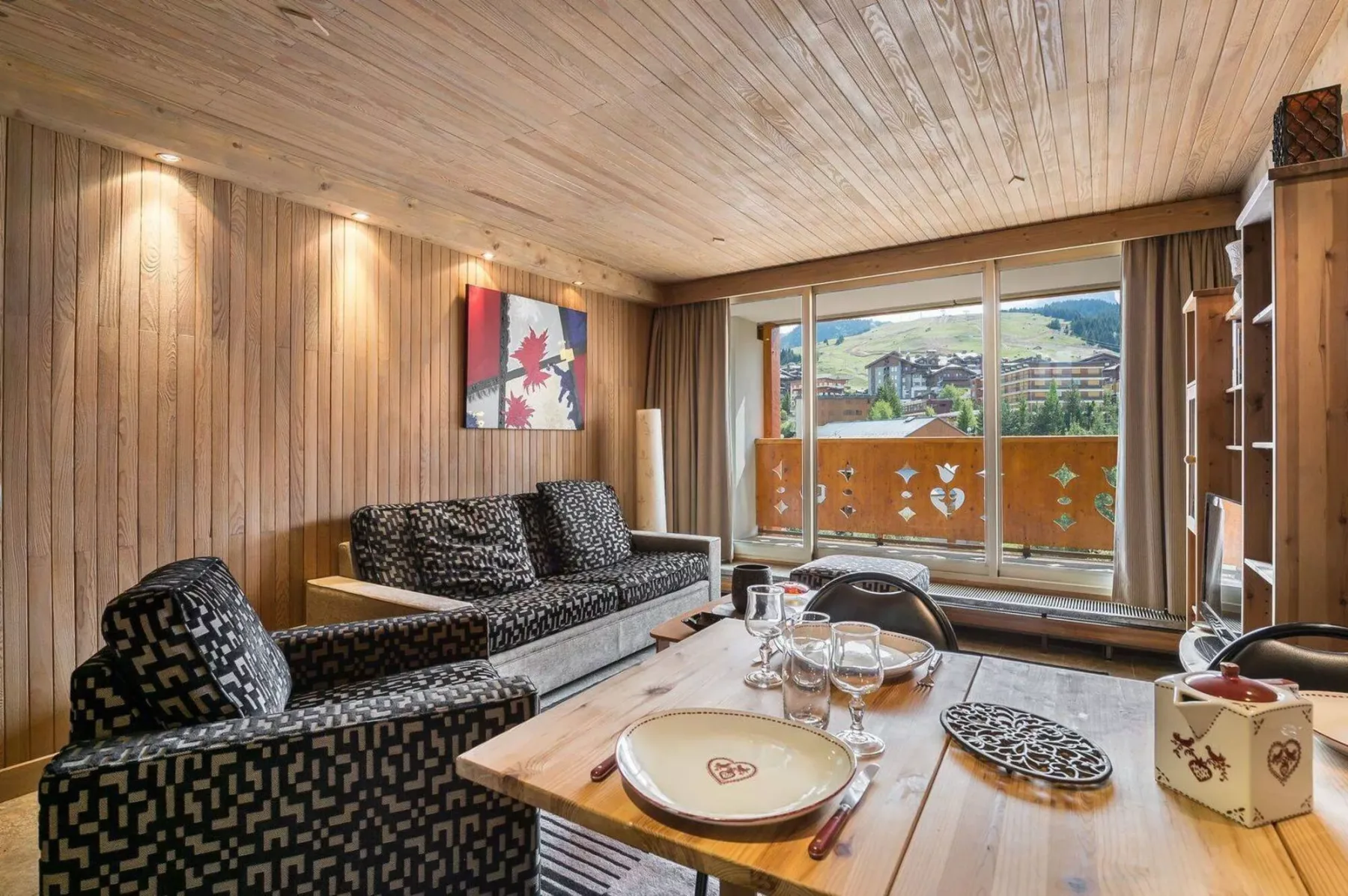 A wood-paneled living room with patterned seating and large windows overlooking a balcony.