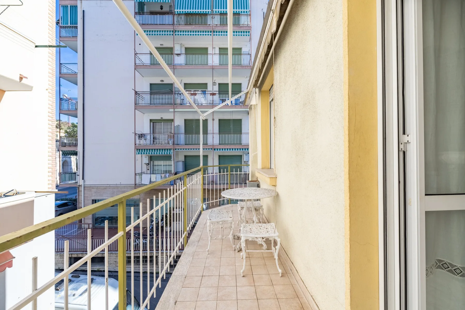 A narrow balcony with tiled flooring and metal railings overlooks nearby apartment buildings.