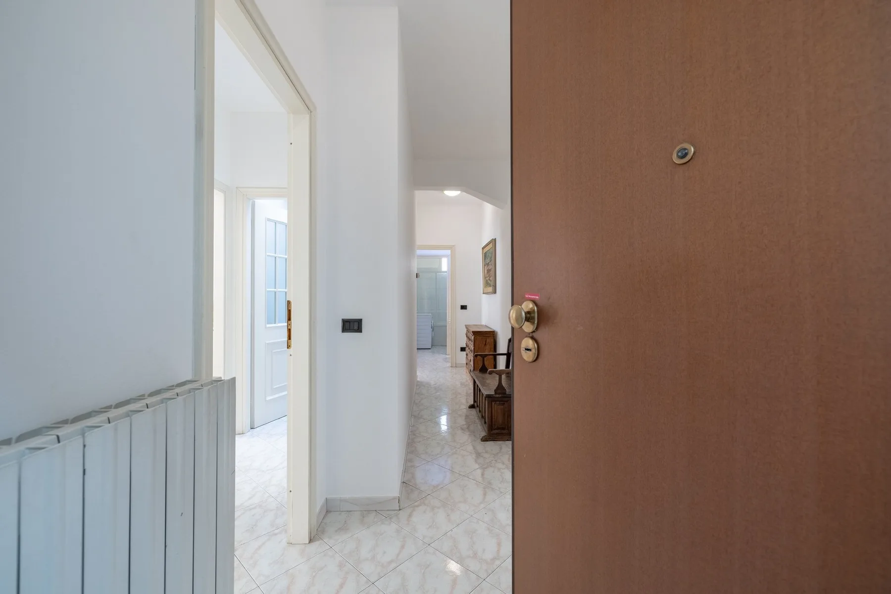 A bright interior hallway with an open wooden entrance door and tiled floors.