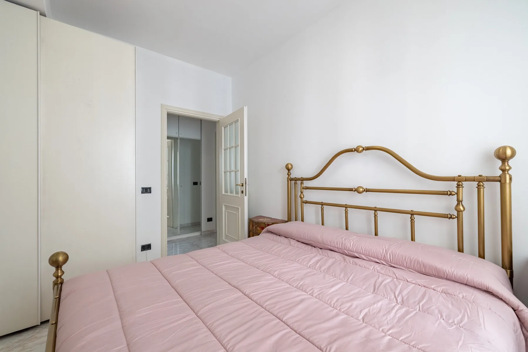 A bedroom with a pink bedspread and a brass-colored bed frame.