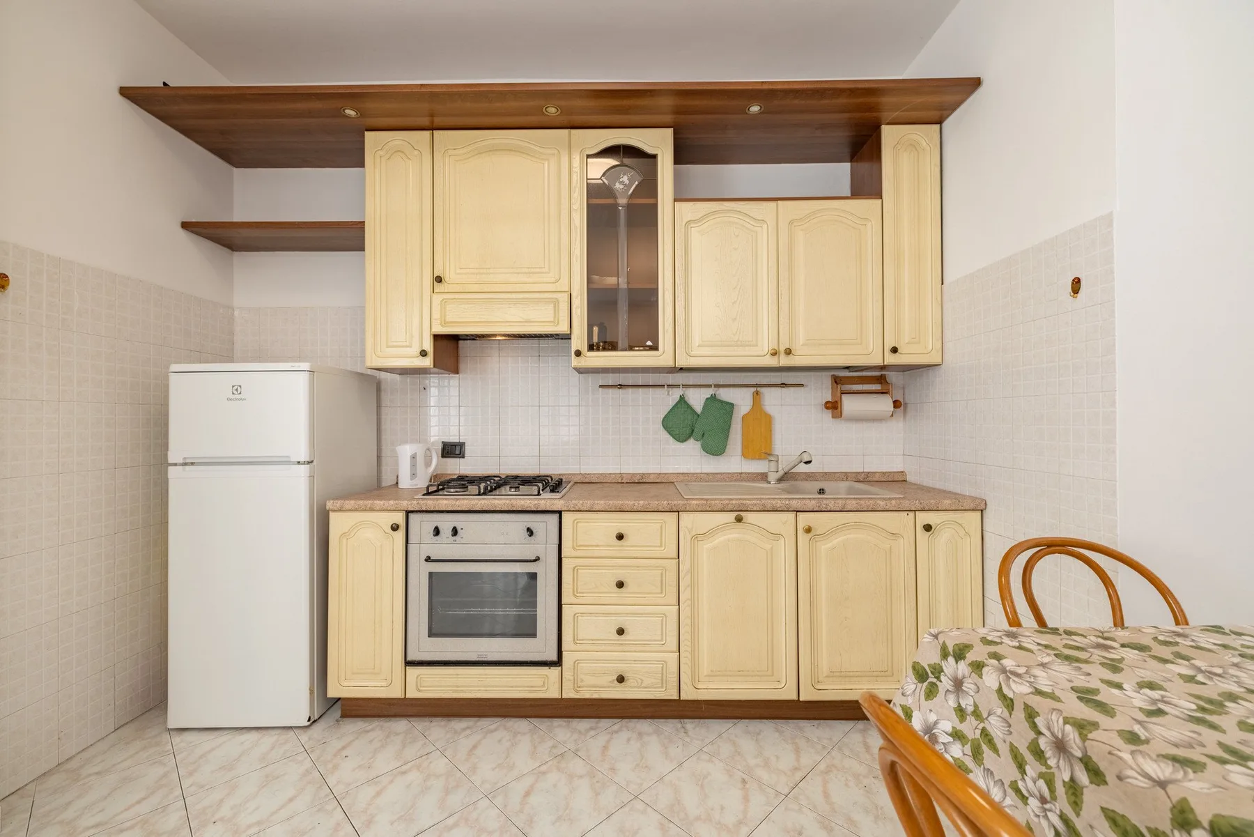 Una cocina con gabinetes claros, un refrigerador y una mesa en primer plano.