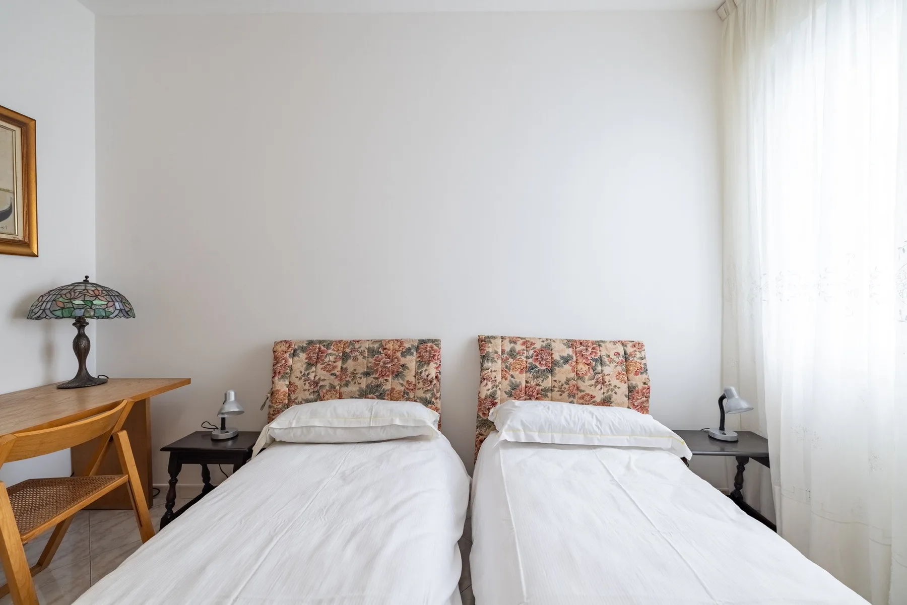 A bedroom with two beds, bedside tables, and a bright window.