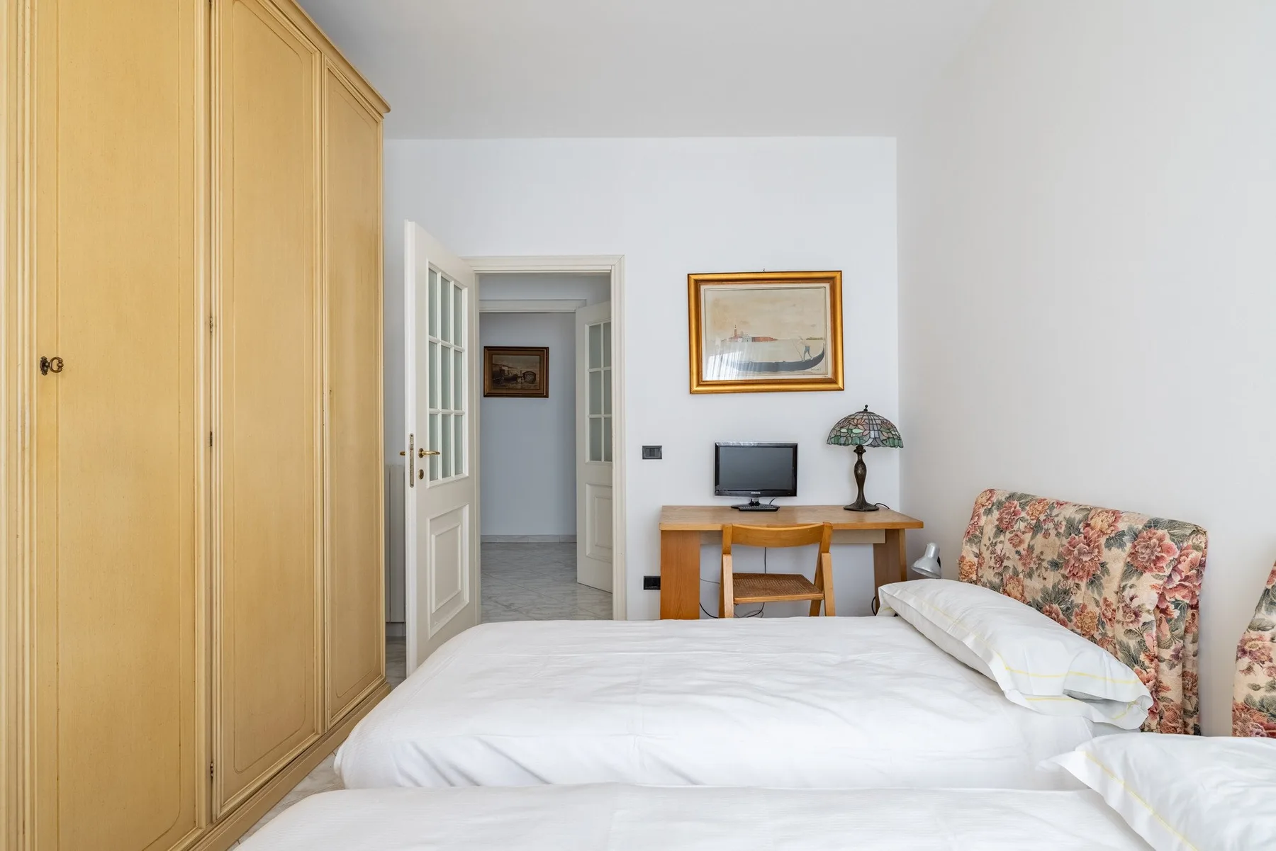 A bright bedroom with a large bed, wooden wardrobes, and a desk.