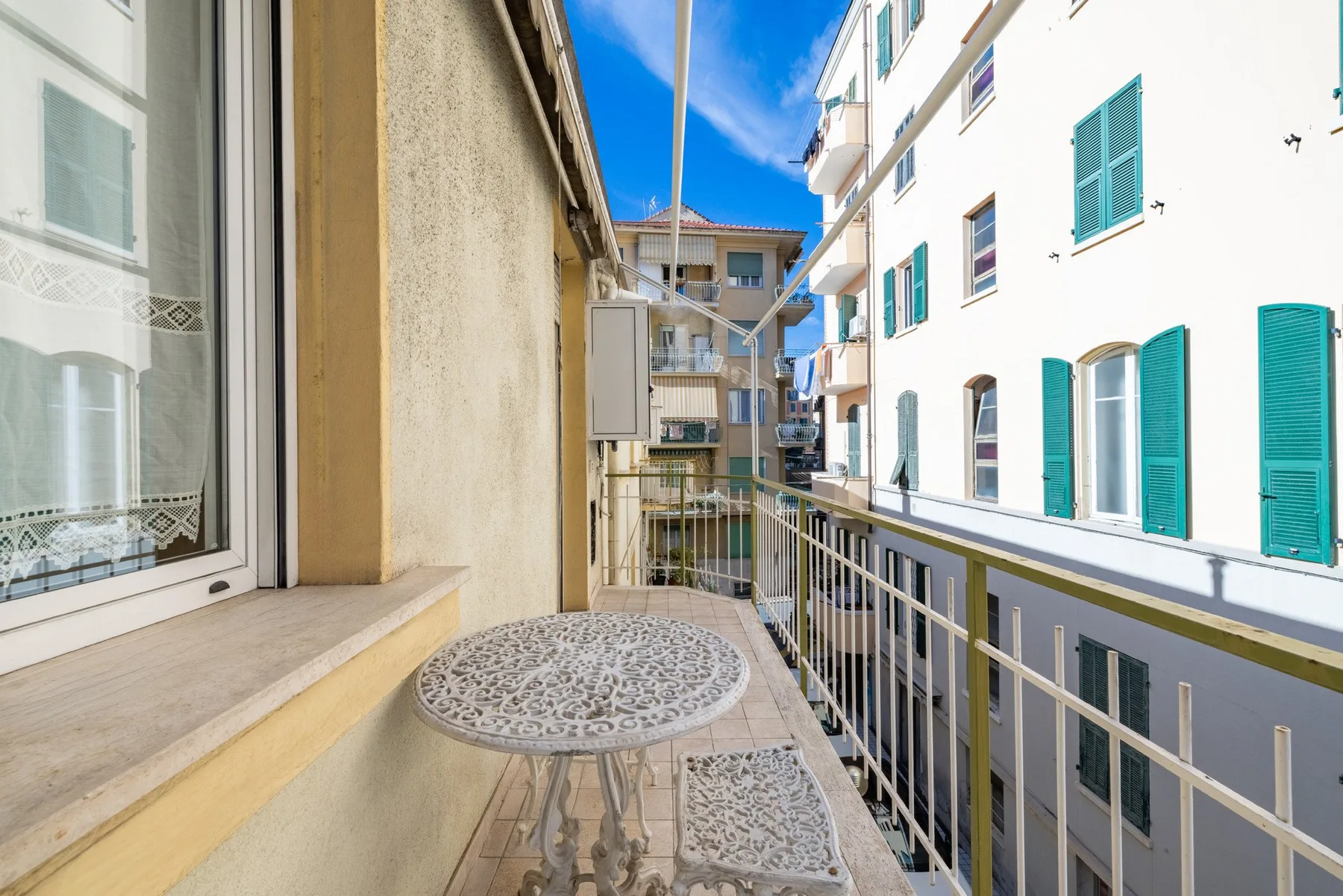 A narrow balcony overlooks neighboring buildings, with a small patterned table in the foreground.