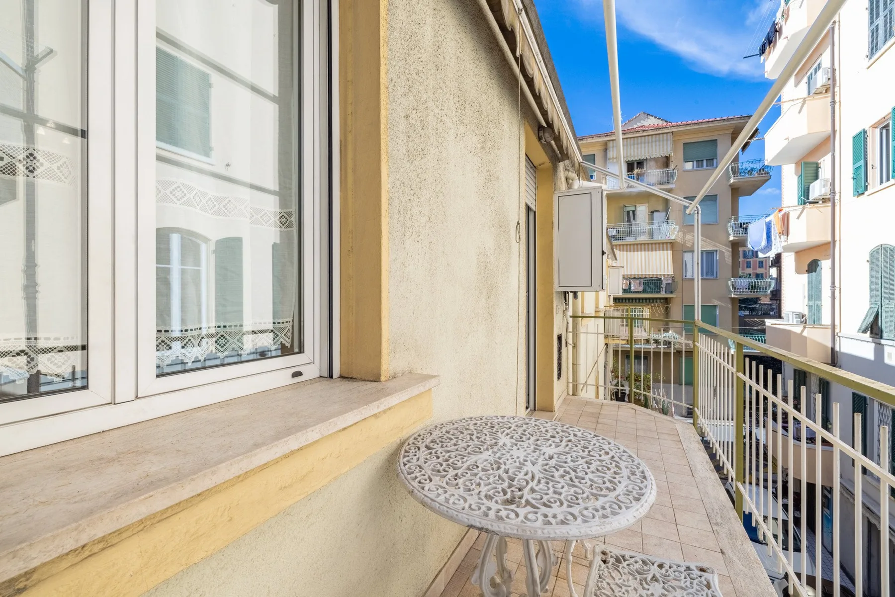 A narrow balcony with a small round table overlooks neighboring apartment buildings.